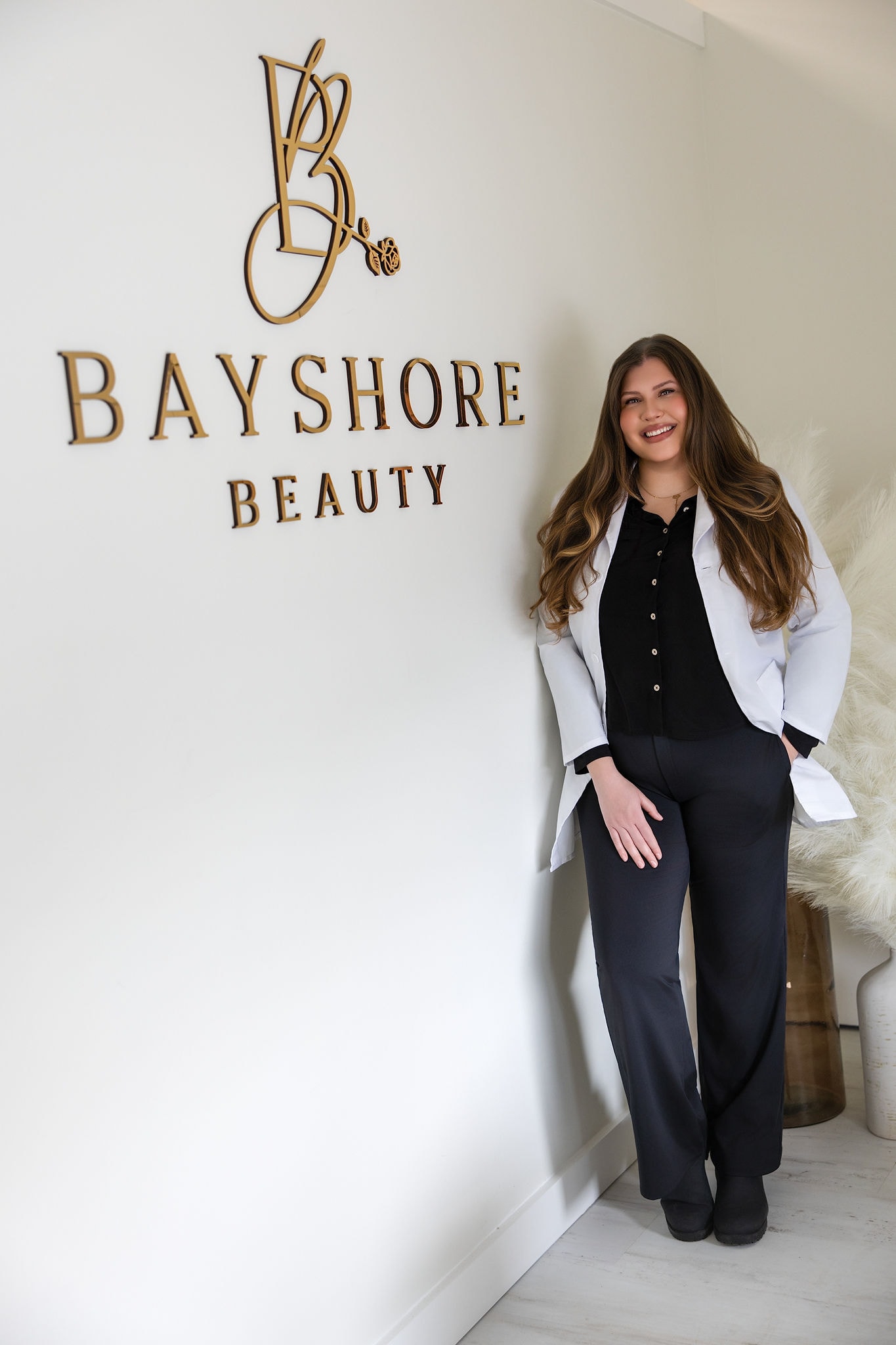 Bayshore Beauty professional beside the studio wall logo